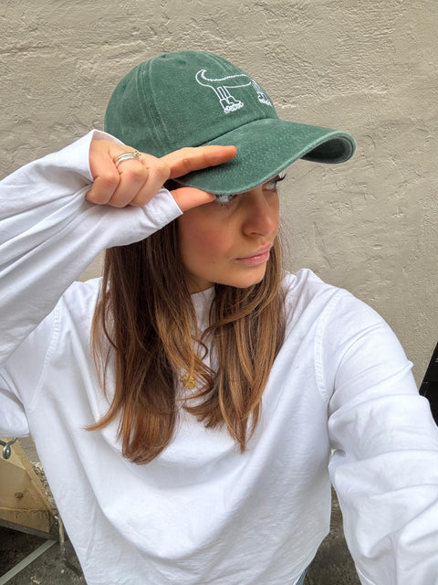 Person wearing a green cap and white sweatshirt against a neutral background