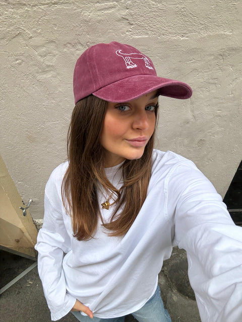 Girl wearing a maroon cap with a logo against a beige wall.